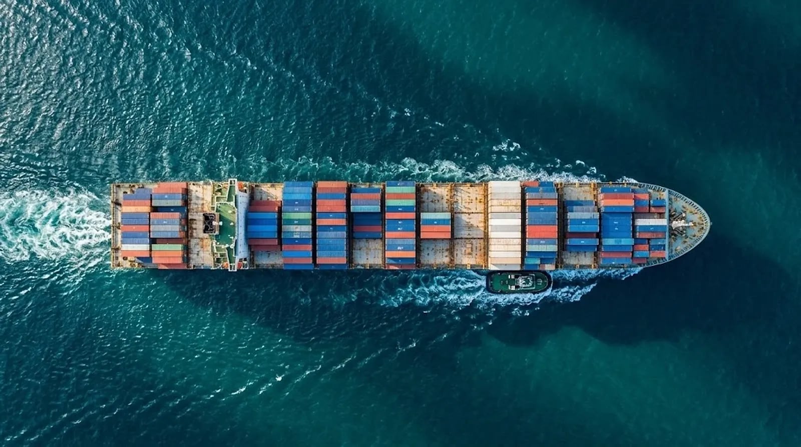 Aerial view of a loaded container ship at sea with a tug alongside